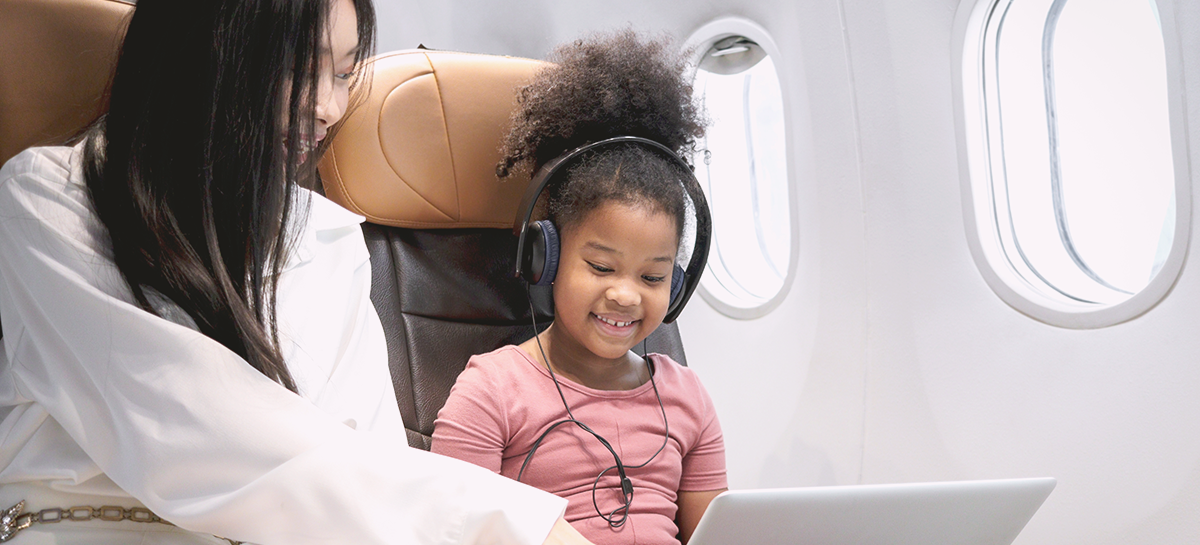 child wearing headphones on plane with parent using laptop